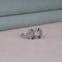 Silver ring with blue accents on a light gray surface, Art Deco Style Sapphire CZ Bridal Ring, Classic Vintage Milgrain Engagement Jewelry Design, Gorgeous Blue Sapphire Fancy CZ Engagement Ring