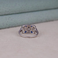 Silver ring with blue stones on a light gray surface, Milgrain Art Deco Vintage Engagement Ring With Round & Blue Sapphire Fancy CZ Stone, Art Deco Sapphire Blue CZ Bridal Jewelry