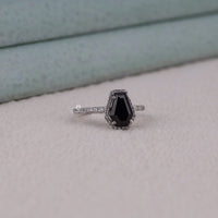 Ring with a black gemstone and diamond-studded band on a light gray surface