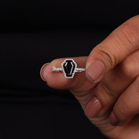 Hand holding a ring with a black gemstone and diamond accents against a dark background