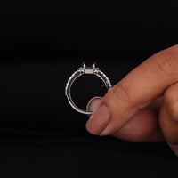 Silver ring held between fingers against a black background