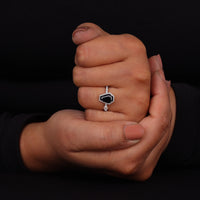 Hand holding a diamond ring with a black gemstone against a dark background