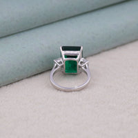Silver ring with green gemstones on a light gray surface, ethical CZ jewelry, vibrant CZ stone ring, green statement ring, colored stone engagement ring, classic three stone ring