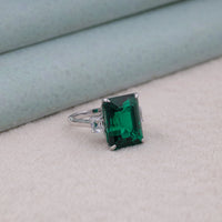 Green gemstone ring on a light gray surface, Affordable Emerald Cut CZ Ring, Green and White Gemstone Ring, emerald cut CZ ring, green and white CZ ring, trilogy gemstone ring, three stone CZ ring, emerald cut engagement ring