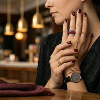 Woman wearing multiple rings and a watch, with a blurred background of a restaurant.