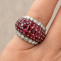 Ring with red gemstone and diamond accents on a finger against a neutral background
