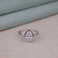 Silver ring with a large diamond on a light gray surface, Bezel Set Oval Solitaire Wedding Ring, Split Shank Modern Engagement Jewelry