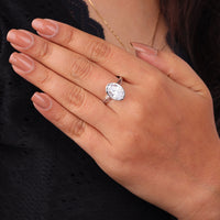Close-up of a hand wearing a silver ring with a large diamond on a dark background, Oval Solitaire Engagement Ring, Bezel Set Split Shank Modern Wedding Band