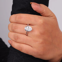 Hand wearing a silver ring with a large gemstone on a plain background, Modern Bezel Set Oval Solitaire Ring, Split Shank Engagement & Wedding Band