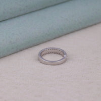 Silver ring with small diamonds on a light beige surface, Moissanite half eternity band, double row Moissanite ring, round cut Moissanite band, 14K gold Moissanite ring, classic Moissanite wedding band, Moissanite anniversary band, stackable Moissanite ring, ethical diamond band