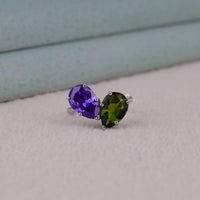 Pair of stud earrings with purple and green gemstones on a light background