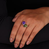 Hand wearing a ring with a purple gemstone on a black background