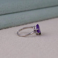 Silver ring with a purple gemstone on a light gray surface