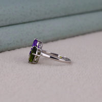 Silver ring with purple and green gemstones on a light gray surface
