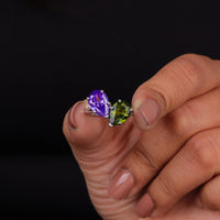 Hand holding a purple and green gemstone against a black background