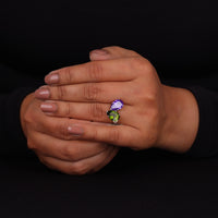 Hand wearing a ring with a purple and green gemstone on a black background