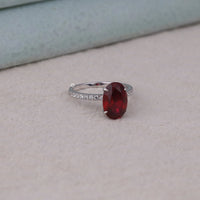 Silver ring with a red gemstone on a light gray surface, Deep Red Cubic Zirconia Engagement Jewelry, Affordable Garnet Oval Promise Ring, Elegant Red Gemstone Bridal Jewelry