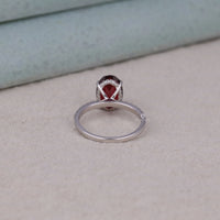 Silver ring with a red gemstone on a light gray surface, Eco Friendly Garnet Style Bridal Ring, Stunning Garnet Oval Halo Ring For Bride, Stylish Red Gemstone Engagement Jewelry.