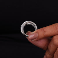 Hand holding a silver ring with intricate design against a black background