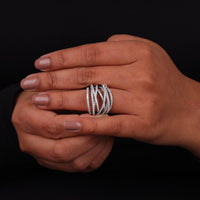 Hand wearing a silver ring with multiple bands on a black background