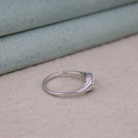 Silver ring with a small diamond on a beige surface, Flush Set Oval Moissanite Engagement Ring, Modern Solitaire Wedding Ring