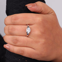 Hand wearing a silver ring with a clear gemstone on a neutral background, Minimalist Oval Moissanite Solitaire Ring, Flush Setting Engagement Jewelry