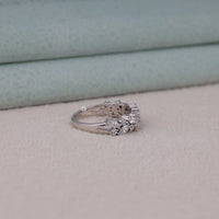 Silver ring with floral design and embedded stones on a light gray surface.