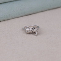 Silver ring with a small bell and leaf design on a beige surface, Sleepy Eevee Cartoon Themed Engagement Ring, Unique Kawaii Anime Ring For Friends, Fun & Whimsical Pokémon Jewelry Design.