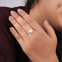Close-up of a hand wearing a pearl ring with a blurred background, pearl bridal ring, Moissanite leaf motif ring, pearl fine jewelry, nature-inspired ring, elegant Moissanite jewelry, Moissanite dainty ring, Moissanite leaf design band, ethical Moissanite ring, pearl fashion ring, Moissanite and leaf ring