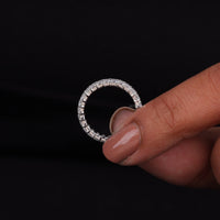 Silver ring with small stones held by a hand against a black background