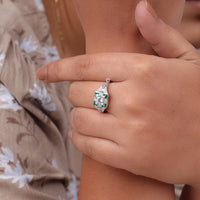 Close-up of a hand wearing an emerald and diamond ring, Edwardian style engagement ring, Art Deco vintage ring, engraved shank ring, filigree detail ring, 1920s inspired ring, antique style jewelry, vintage wedding ring, heirloom inspired ring, historical jewelry design