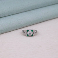 Silver ring with green gemstones on a light gray surface, filigree Edwardian jewelry, engraved Art Deco band, romantic antique engagement ring, ornate vintage style ring, antique reproduction ring