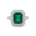 Ring with emerald-cut green gemstone and diamond accents on a white background