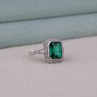 Ring with a green gemstone and diamond-studded band on a light gray surface.