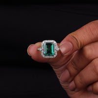 Ring with a green gemstone held between fingers against a black background