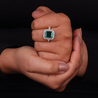Hand holding a ring with a green gemstone against a black background