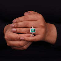 Hand wearing a ring with a green gemstone on a black background