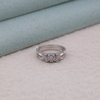 Silver ring with floral design on a light gray surface, heirloom style moissanite rings, moissanite wedding jewelry, art deco bridal ring set, round cut moissanite wedding band, timeless moissanite engagement ring, bridal ring vintage inspired