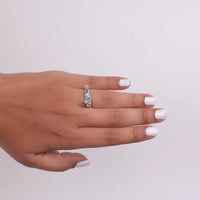 Hand wearing a silver ring with a clear stone on a light gray background, round moissanite bridal set, vintage style wedding ring, moissanite engagement ring set, antique inspired bridal jewelry, moissanite wedding band set, sustainable wedding rings, vintage moissanite ring set, bridal ring set for her, classic wedding ring set