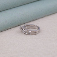 Two silver rings stacked on a textured surface with a light blue background, ethical bridal jewelry, round moissanite wedding set, vintage ring for engagement, moissanite vintage wedding set, romantic moissanite ring set