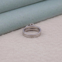 Silver ring pendant on a textured surface with a light green background, bridal jewelry set, detailed moissanite band, two piece moissanite ring set, ornate bridal set moissanite, non diamond wedding ring set