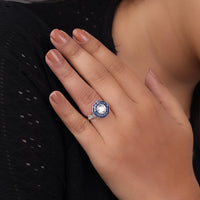 Close-up of a hand wearing a decorative ring with a blue gemstone on a dark background, Vintage Style Engagement Ring, Round CZ Halo Ring