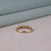 Gold ring with embedded stones on a light surface, Emerald and Round Cut Moissanite Band – Bezel Set Seven Stone Wedding Jewelry