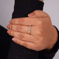 Hand wearing a diamond ring on a neutral background,  Seven Stone Moissanite Eternity Band – Emerald & Round Cut Bezel Set Wedding Ring