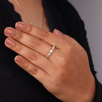 Close-up of a hand wearing a diamond ring on a neutral background, Bezel Set Emerald & Round Moissanite Half Eternity Band – Seven Stone Wedding Ring