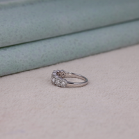 Silver ring with gemstones on a light pink surface, Elegant Seven Stone Halo Moissanite Ring – Round Cut White Gold Engagement Jewelry