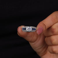 Diamond ring with blue gemstones held between fingers against a black background