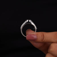 Silver ring held between fingers against a black background