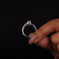 Silver ring with a diamond held by a hand against a black background
