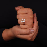 Two hands holding a silver ring with a diamond on a black background